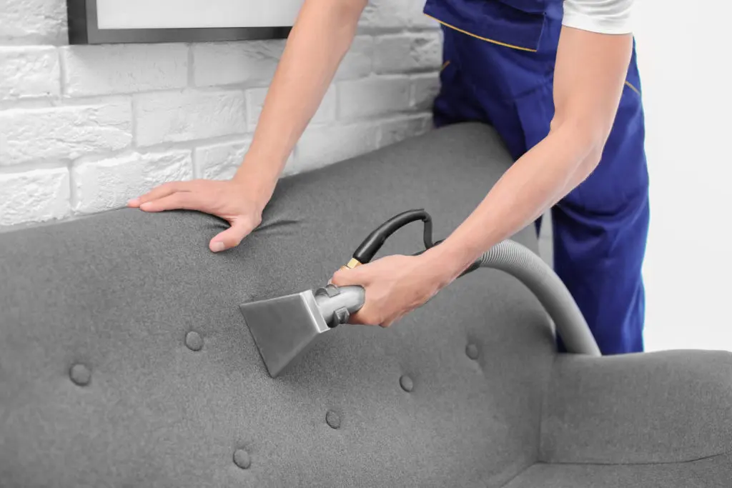 Technician cleaning a fabric sofa cushion with an upholstery tool
